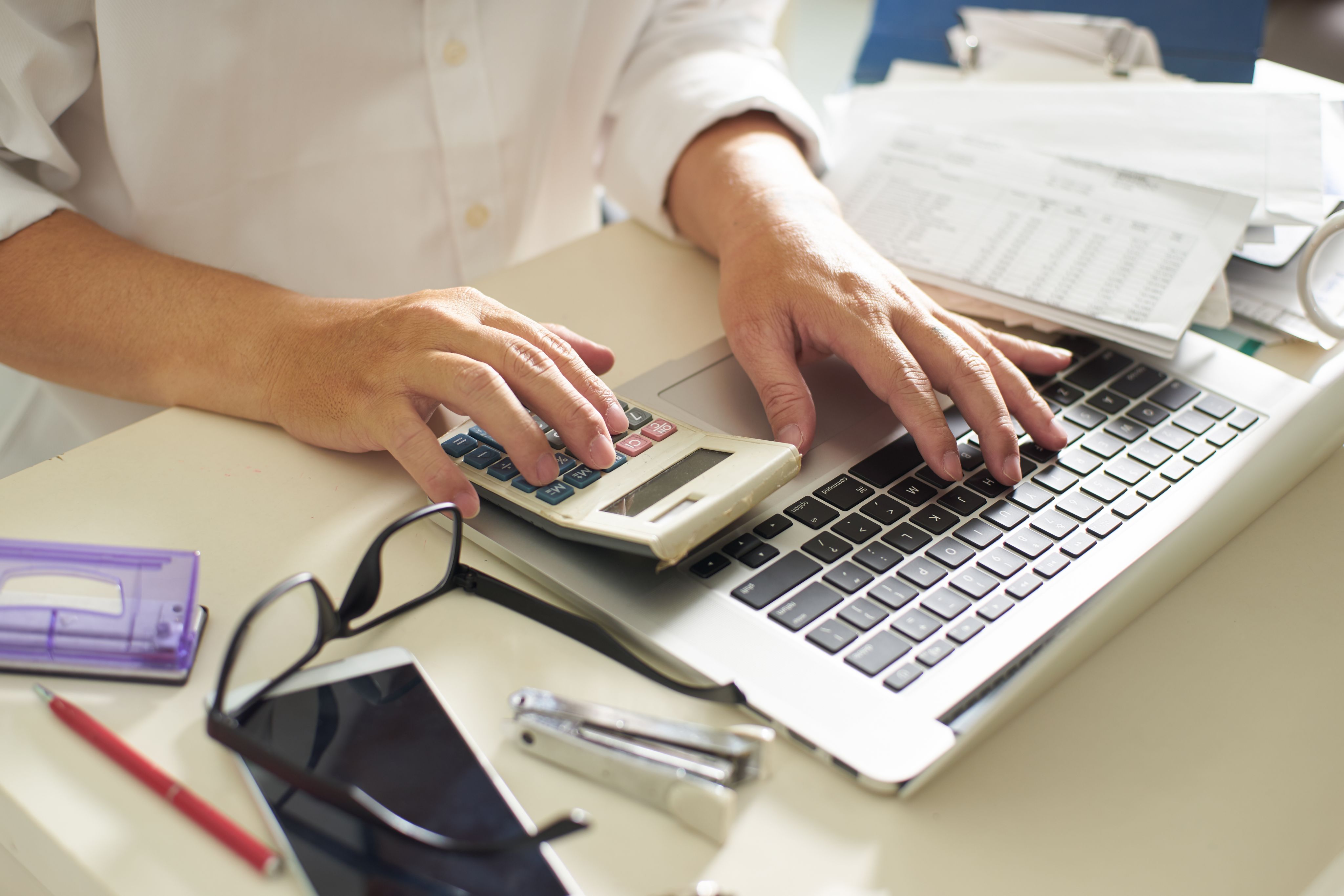 person working at desk with laptop and calculator 